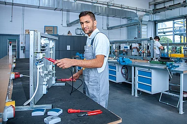 Techniker prüft elektrische Anlage mit Messgerät in einer Werkstatt.