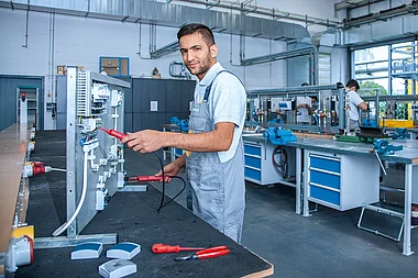 Techniker prüft elektrische Anlage mit Messgerät in einer Werkstatt.