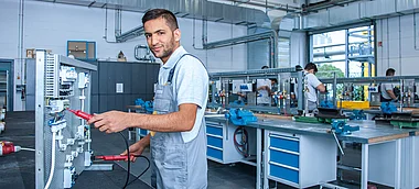 Techniker prüft elektrische Anlage mit Messgerät in einer Werkstatt.