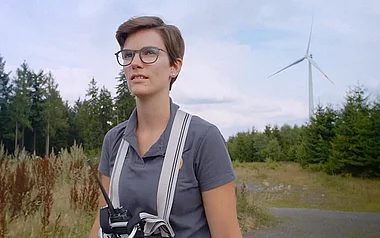 Technikerin inspiziert Gelände mit Funkgerät und Fernglas.