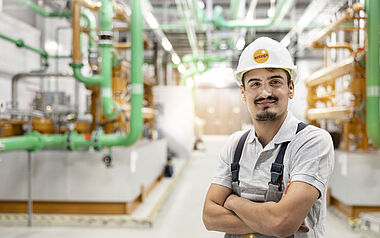 Techniker steht in einer Fabrikhalle mit Rohren im Hintergrund.