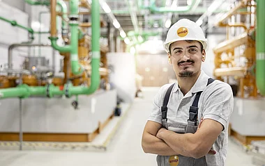 Techniker steht in einer Fabrikhalle mit Rohren im Hintergrund.