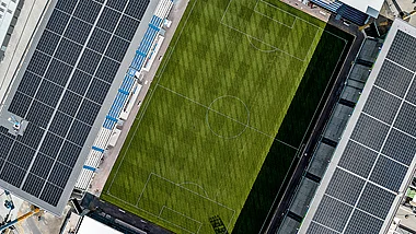 Vogelperspektive zeigt ein Fußballfeld mit Solaranlagen auf dem Stadiondach.