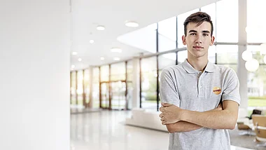 Ein junger Mann steht lächelnd vor einem modernen Bürogebäude.