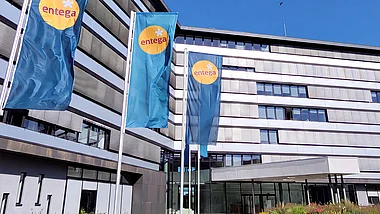 Modernes Bürogebäude der ENTEGA mit Fahnenmasten, Grünflächen und einem blauen Himmel.