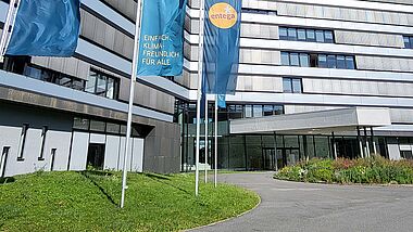 Modernes Bürogebäude der ENTEGA mit Fahnenmasten, Grünflächen und einem blauen Himmel.