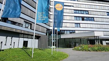 Modernes Bürogebäude der ENTEGA mit Fahnenmasten, Grünflächen und einem blauen Himmel.