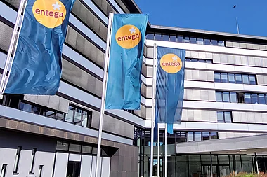 Modernes Bürogebäude der ENTEGA mit Fahnenmasten, Grünflächen und einem blauen Himmel.