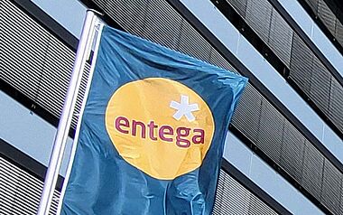 Modernes Bürogebäude der ENTEGA mit Fahnenmasten, Grünflächen und einem blauen Himmel.