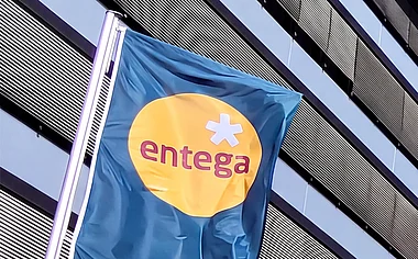 Modernes Bürogebäude der ENTEGA mit Fahnenmasten, Grünflächen und einem blauen Himmel.