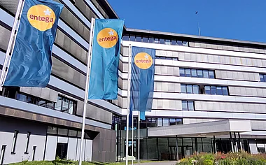 Modernes Bürogebäude der ENTEGA mit Fahnenmasten, Grünflächen und einem blauen Himmel.