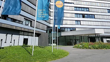 Modernes Bürogebäude der ENTEGA mit Fahnenmasten, Grünflächen und einem blauen Himmel.