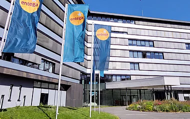 Modernes Bürogebäude der ENTEGA mit Fahnenmasten, Grünflächen und einem blauen Himmel.