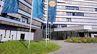 Modernes Bürogebäude der ENTEGA mit Fahnenmasten, Grünflächen und einem blauen Himmel.