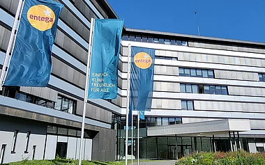 Modernes Bürogebäude der ENTEGA mit Fahnenmasten, Grünflächen und einem blauen Himmel.