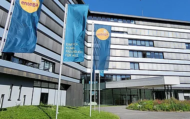 Modernes Bürogebäude der ENTEGA mit Fahnenmasten, Grünflächen und einem blauen Himmel.