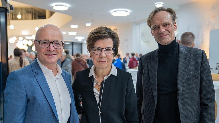 Drei Personen stehen lächelnd in einem modernen, hell erleuchteten Raum.