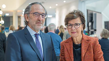 Zwei Personen stehen bei einer Veranstaltung mit Blick auf eine Gruppe von Menschen.
