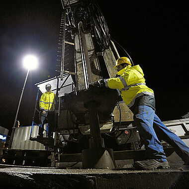 Bauarbeiter bei einer Geothermiebohrung bei Dunkelheit.