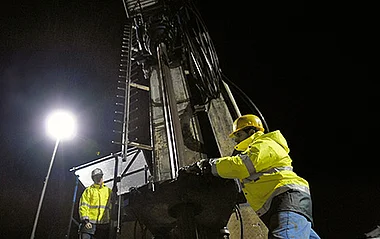 Bauarbeiter bei einer Geothermiebohrung bei Dunkelheit.