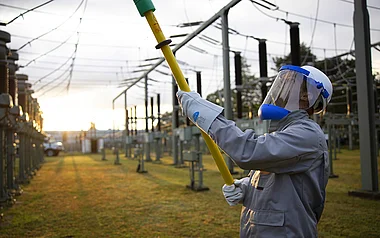 Techniker inspiziert Hochspannungsleitungen bei Sonnenuntergang.