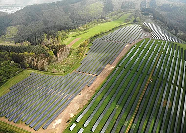 Solarmodule auf einer weitläufigen, sonnendurchfluteten Landschaftsfläche.