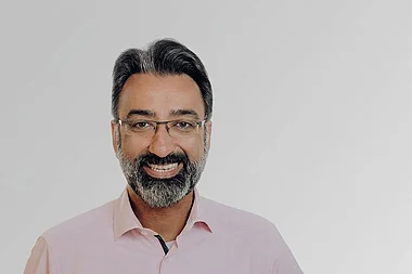 Ein Mann mit Bart und Brille trägt ein rosafarbenes Hemd.