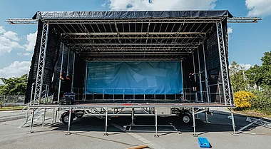 Bühnenaufbau mit Technik und Zubehör auf einem Parkplatz.