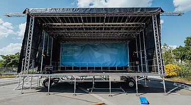 Bühnenaufbau mit Technik und Zubehör auf einem Parkplatz.