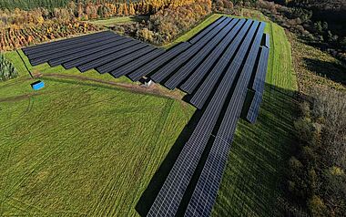 Solarmodule auf einer Hügelkuppe mit Blick auf eine bewaldete Landschaft.