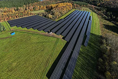 Solarmodule auf einer Hügelkuppe mit Blick auf eine bewaldete Landschaft.
