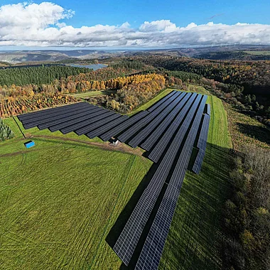 Solarmodule auf einer Hügelkuppe mit Blick auf eine bewaldete Landschaft.