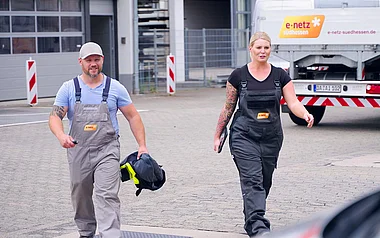 Zwei Mitarbeiter in Arbeitsoveralls tragen Ausrüstung auf einem Firmengelände.