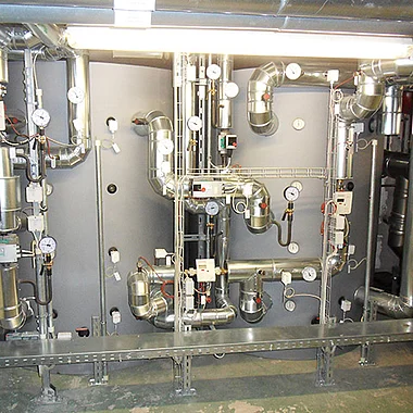 Ventilationsanlage mit Rohren, Ventilen und Messgeräten in einem Technikraum eines Gebäudes.