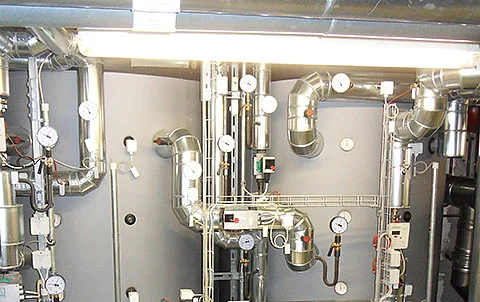 Ventilationsanlage mit Rohren, Ventilen und Messgeräten in einem Technikraum eines Gebäudes.