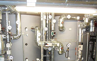 Ventilationsanlage mit Rohren, Ventilen und Messgeräten in einem Technikraum eines Gebäudes.