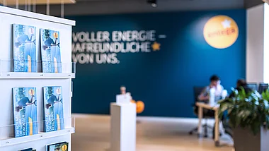 Moderne Büroräume mit Mitarbeitern und Pflanzen im Hintergrund.