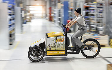 Lieferkurier transportiert Waren mit einem Lastenfahrrad durch ein Lager.