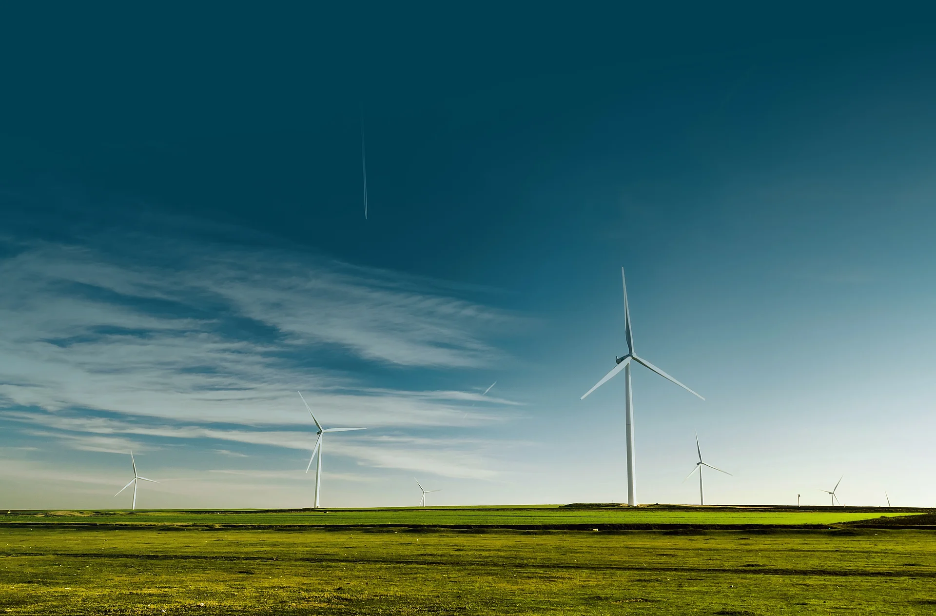 Windräder stehen auf einer grünen Hügelkuppe vor einem bewölkten Himmel.