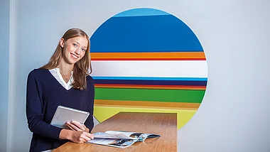 Eine Person hält ein Tablet und blickt freundlich in die Kamera.