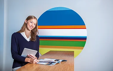 Eine Person hält ein Tablet und blickt freundlich in die Kamera.