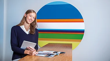 Eine Person hält ein Tablet und blickt freundlich in die Kamera.