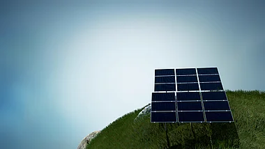 Solarmodule auf einer grünen Hügelkuppe unter blauem Himmel.