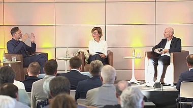 Zwei Redner diskutieren vor einem Publikum auf einer Konferenz.