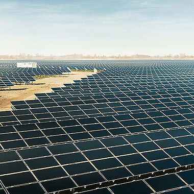 Solarmodule auf einer weitläufigen, sonnendurchfluteten Landschaftsfläche.