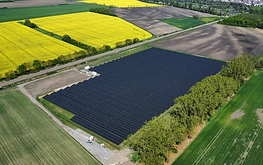 Solarpark mit zahlreichen Modulen und angrenzenden Feldern aus der Vogelperspektive.