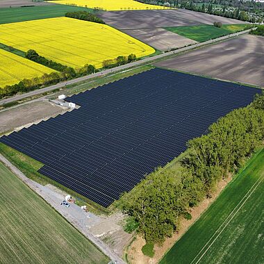 Solarpark mit zahlreichen Modulen und angrenzenden Feldern aus der Vogelperspektive.