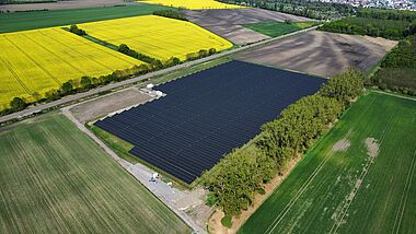 Solarpark mit zahlreichen Modulen und angrenzenden Feldern aus der Vogelperspektive.