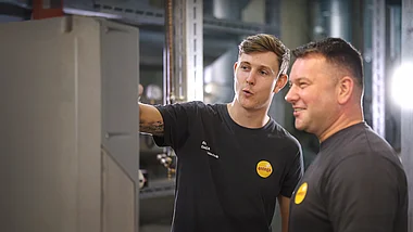 Techniker zeigt einen Mitarbeiter einen Prozessablauf in einer Produktionshalle.