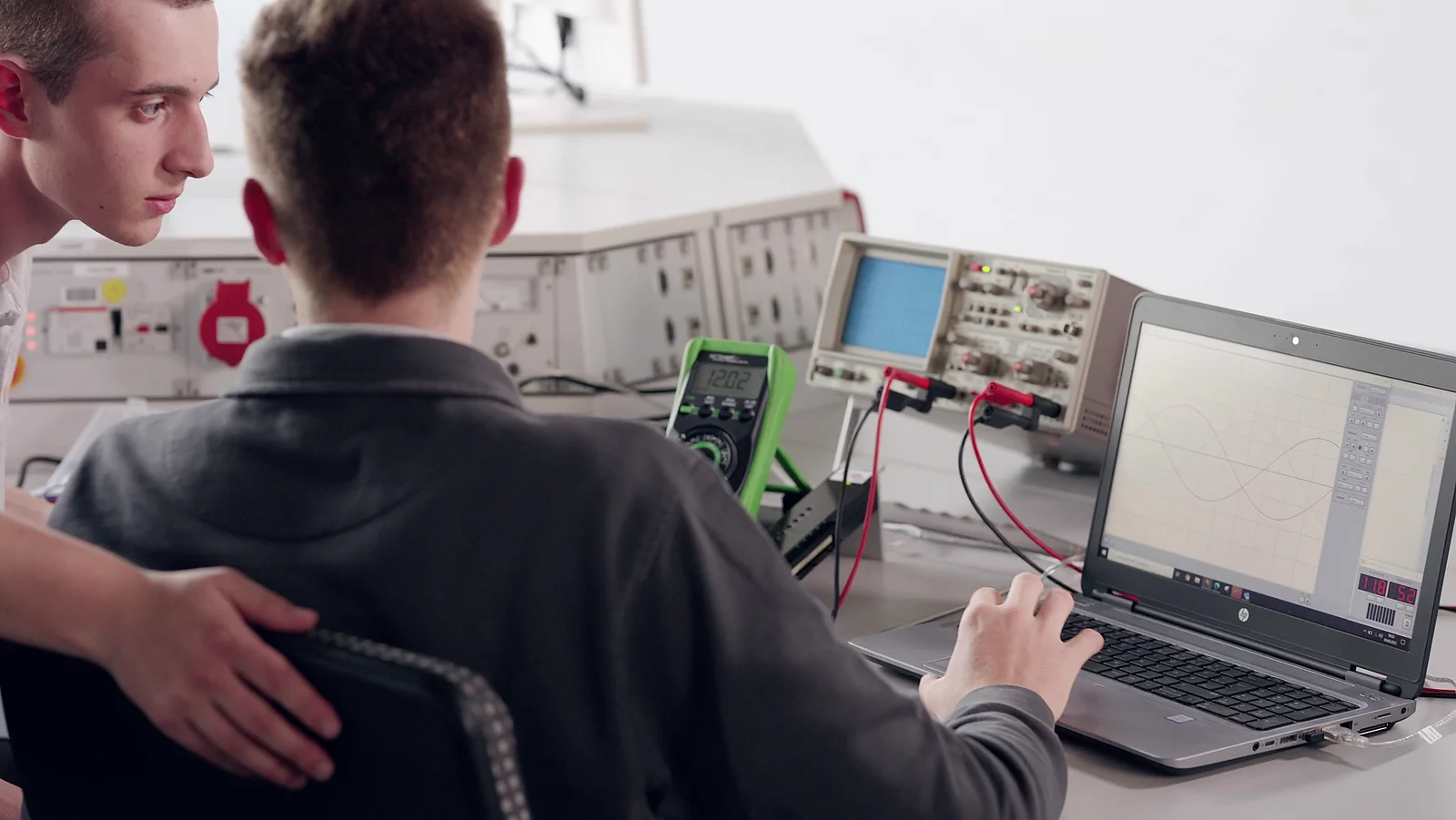 Techniker analysiert Schaltkreise mit Messgeräten und Laptop.